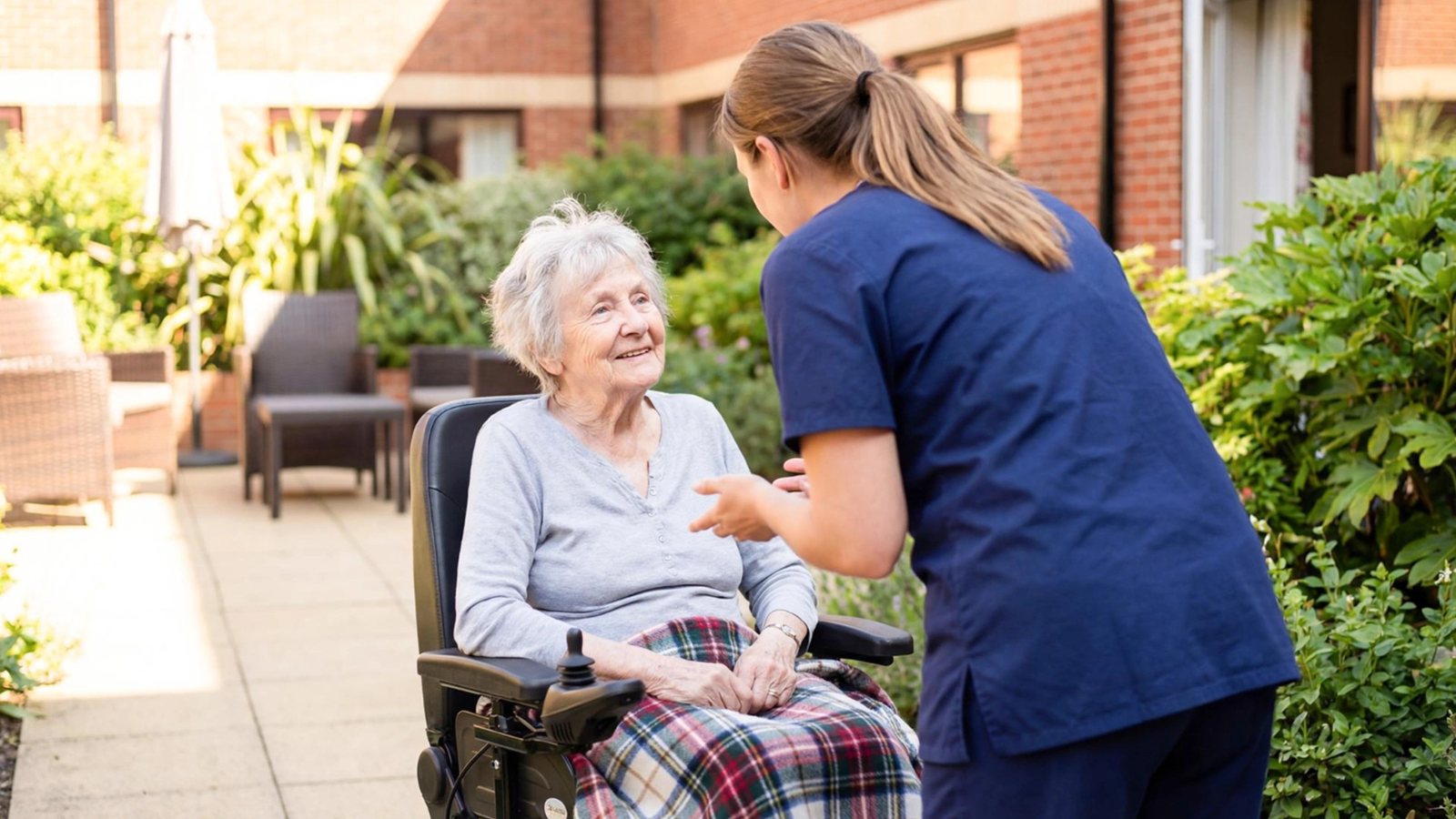 A nurse crouching to talk with a resident in her wheelchair in the garden